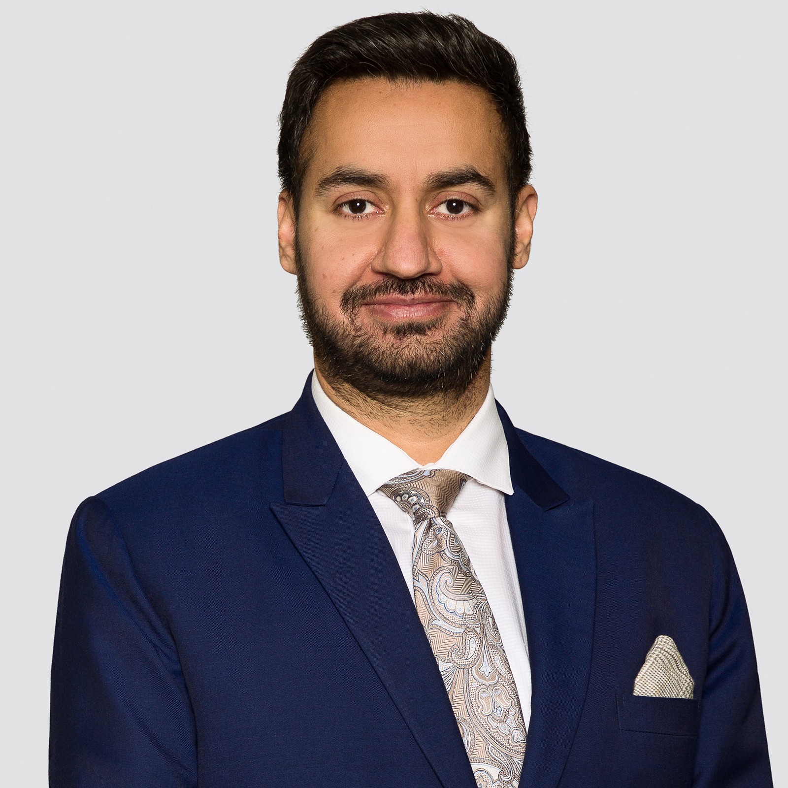 headshot of a man of south asian decent, bearded and dark hair wearing a blue suit jacket and white collared shirt
